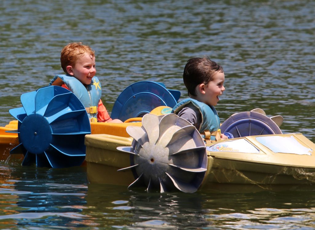 Two children in paddleboats on a lake.