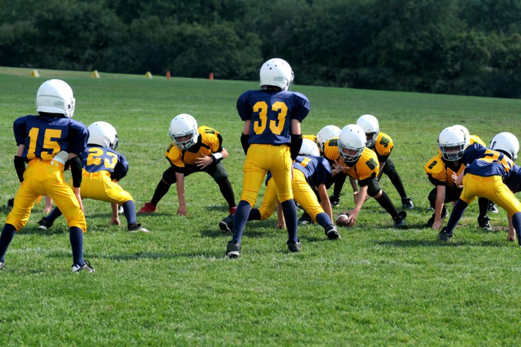 Children playing football in navy and gold uniforms and white helmets.